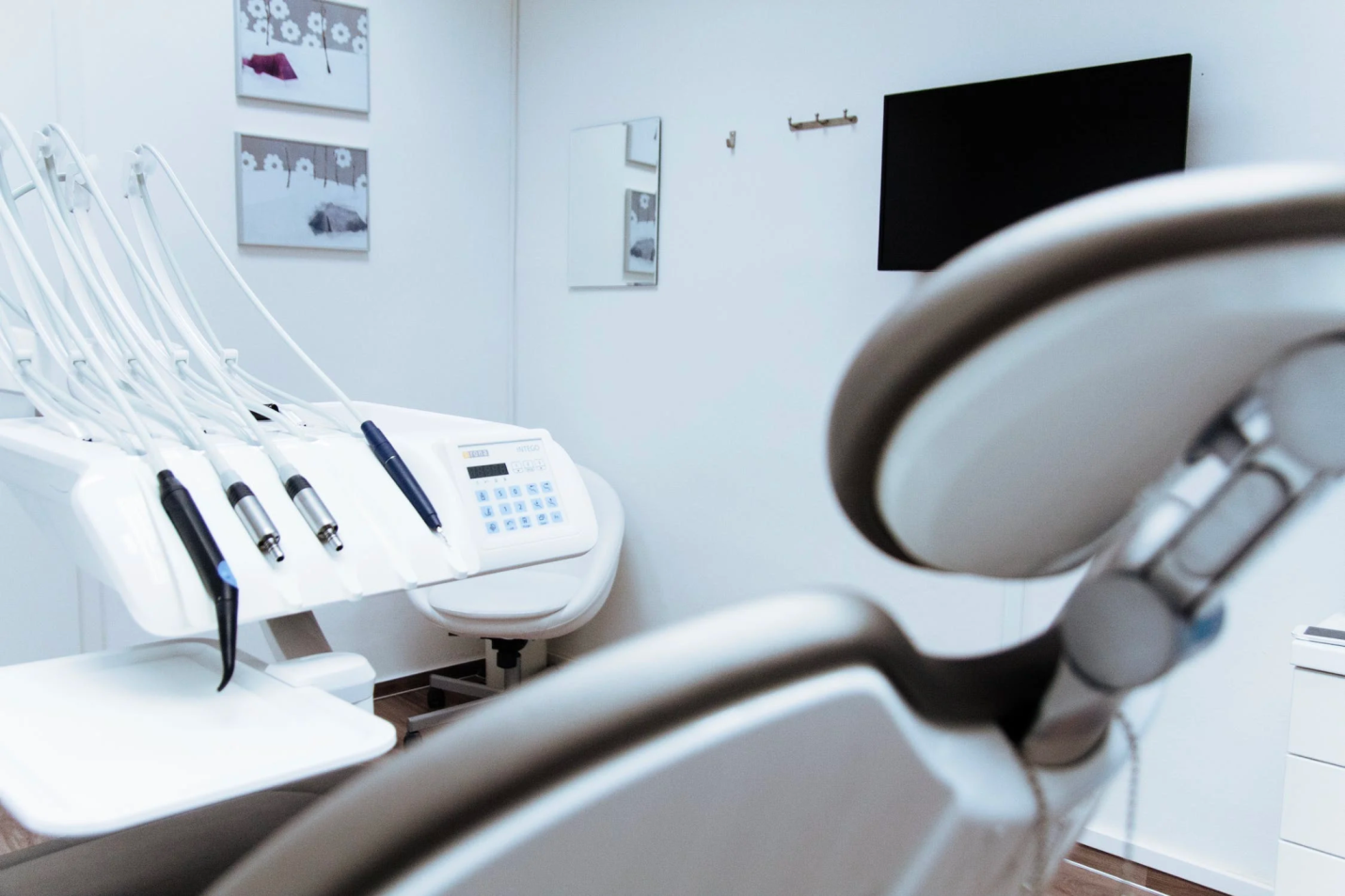 A dental chair with tools and a monitor on the wall inside an office.